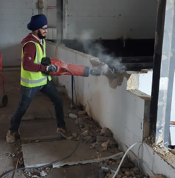 An image of a worker using a power drill to break up concrete blocks of a wall.